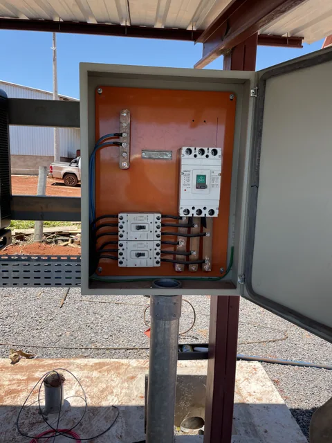 Quadro de comando aberto com componentes elétricos fixados em placa laranja