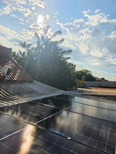 Painéis solares sobre telhado com luz do sol e árvores ao fundo